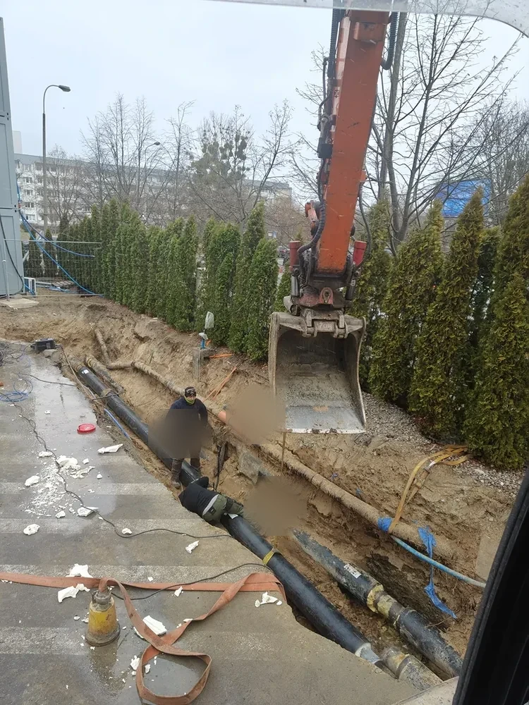 Układanie przyłącza Koparka układająca rury w wykopie pod przyłącze wśród zieleni