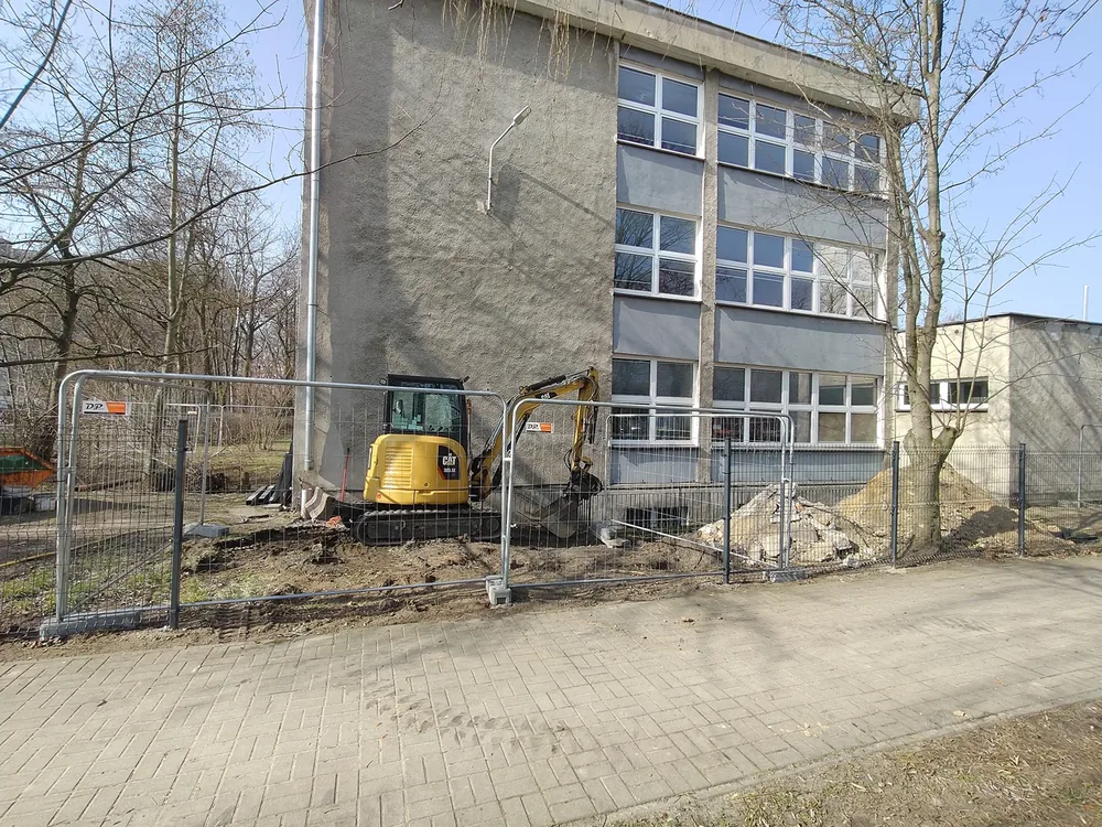 Praca minikoparką Minikoparka wykonująca prace na ciasnej działce przy ogrodzeniu