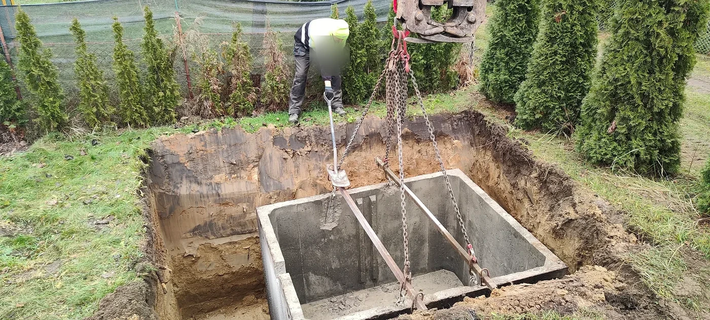 Montaż zbiornika na szambo Betonowy zbiornik opuszczany dźwigiem do wykopu na szambo w ogrodzie